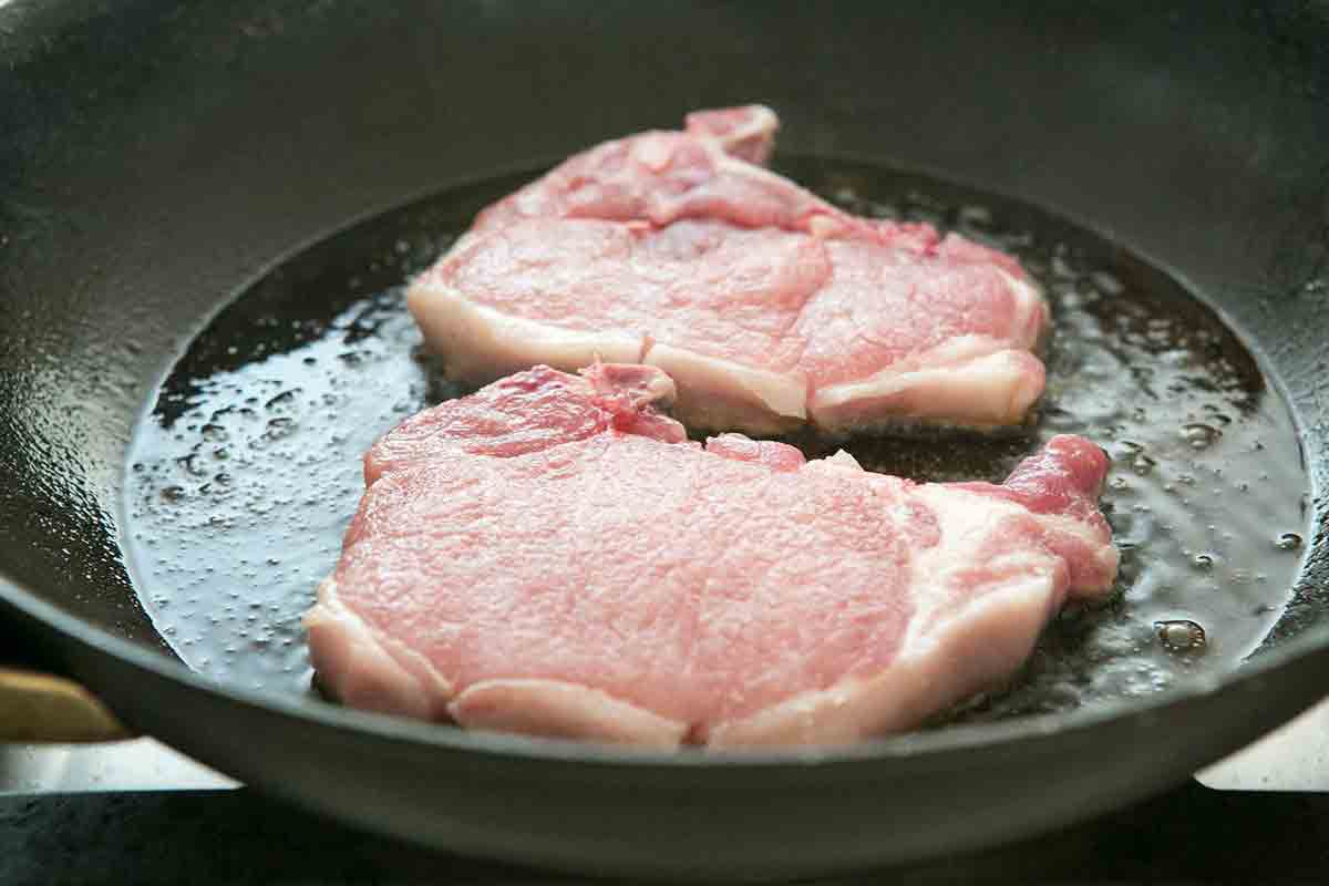 two pork chops cooking in pan