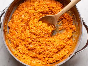 A skillet containing orzo pasta mixed with a creamy vodkabased sauce stirred with a wooden spoon