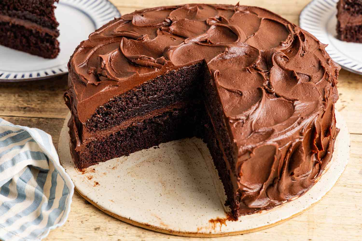 black magic cake on a platter with a slice cut out and in the background, two plates with some cake slices