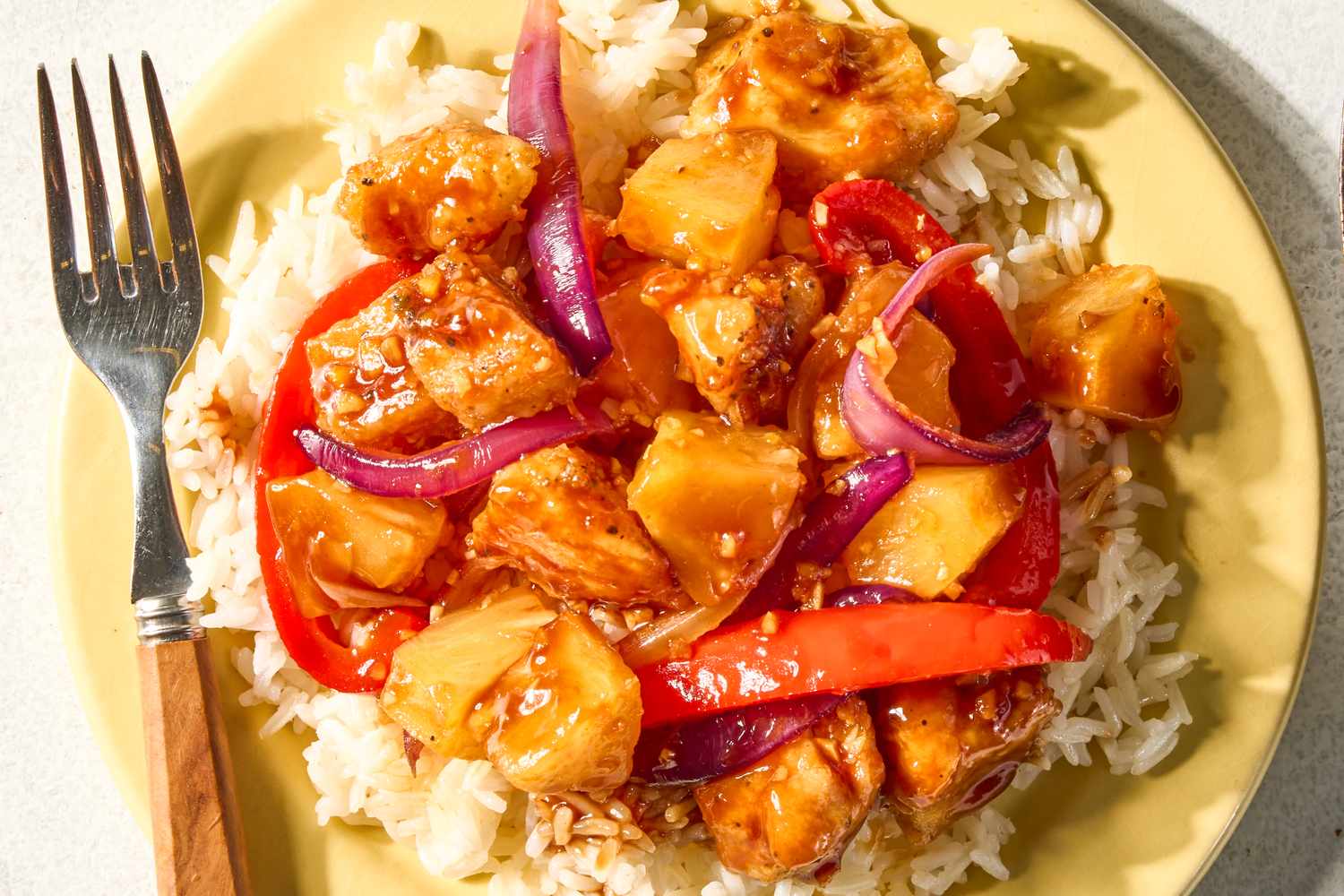 Pineapple chicken served on a bed of rice garnished with red bell peppers and onions