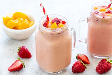 Strawberry peach smoothie with a straw and chopped fruit on top and around the glass cup.