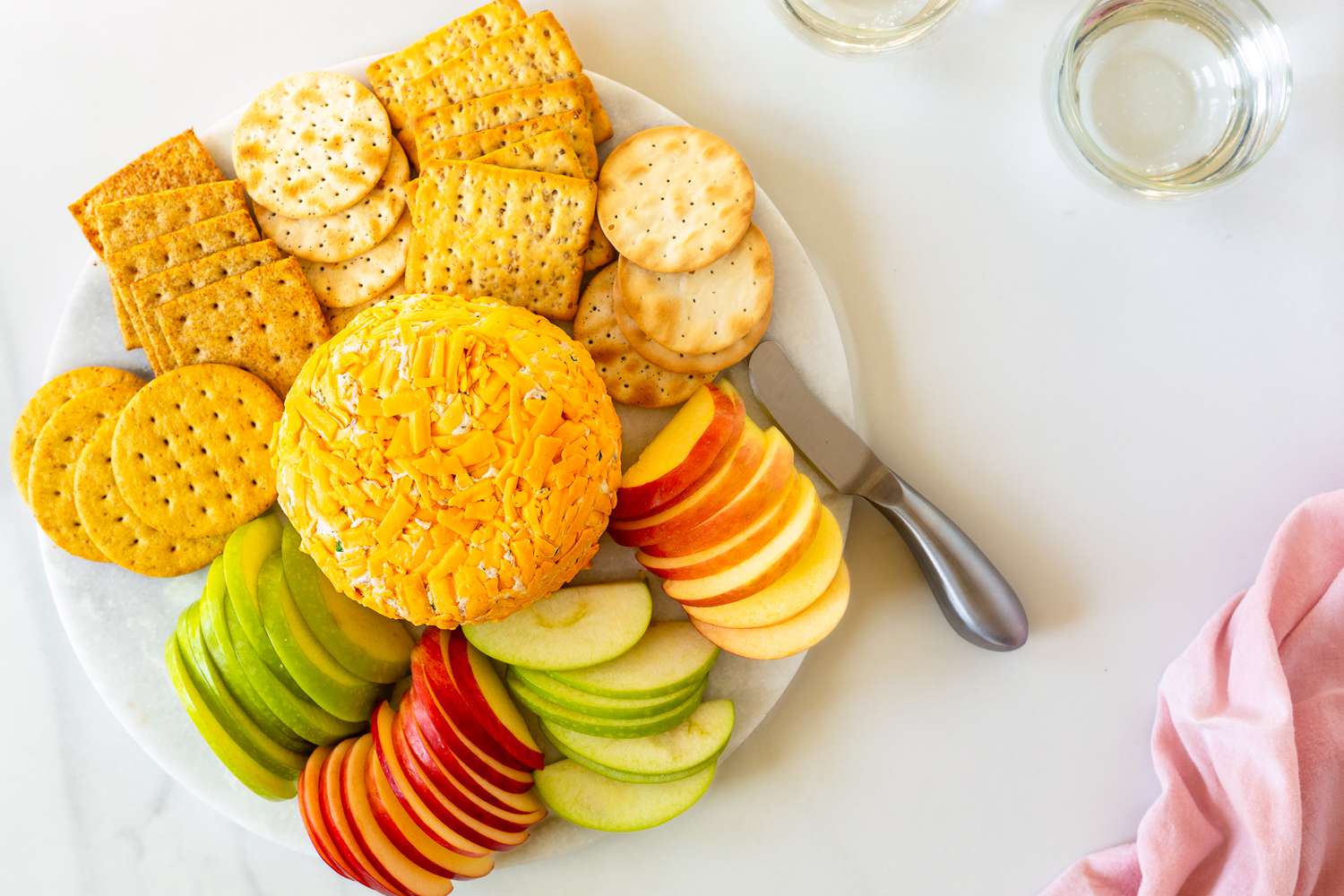 Overhead view of a white plate of a ham ball appetizer surrounded by various crackers and apple slices