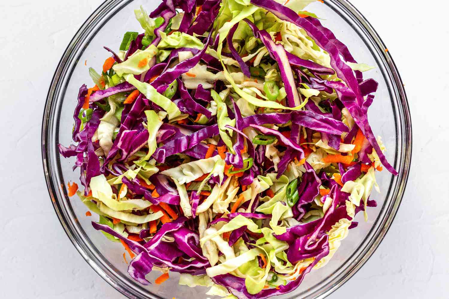 Sliced green and purple cabbage in a glass bowl.