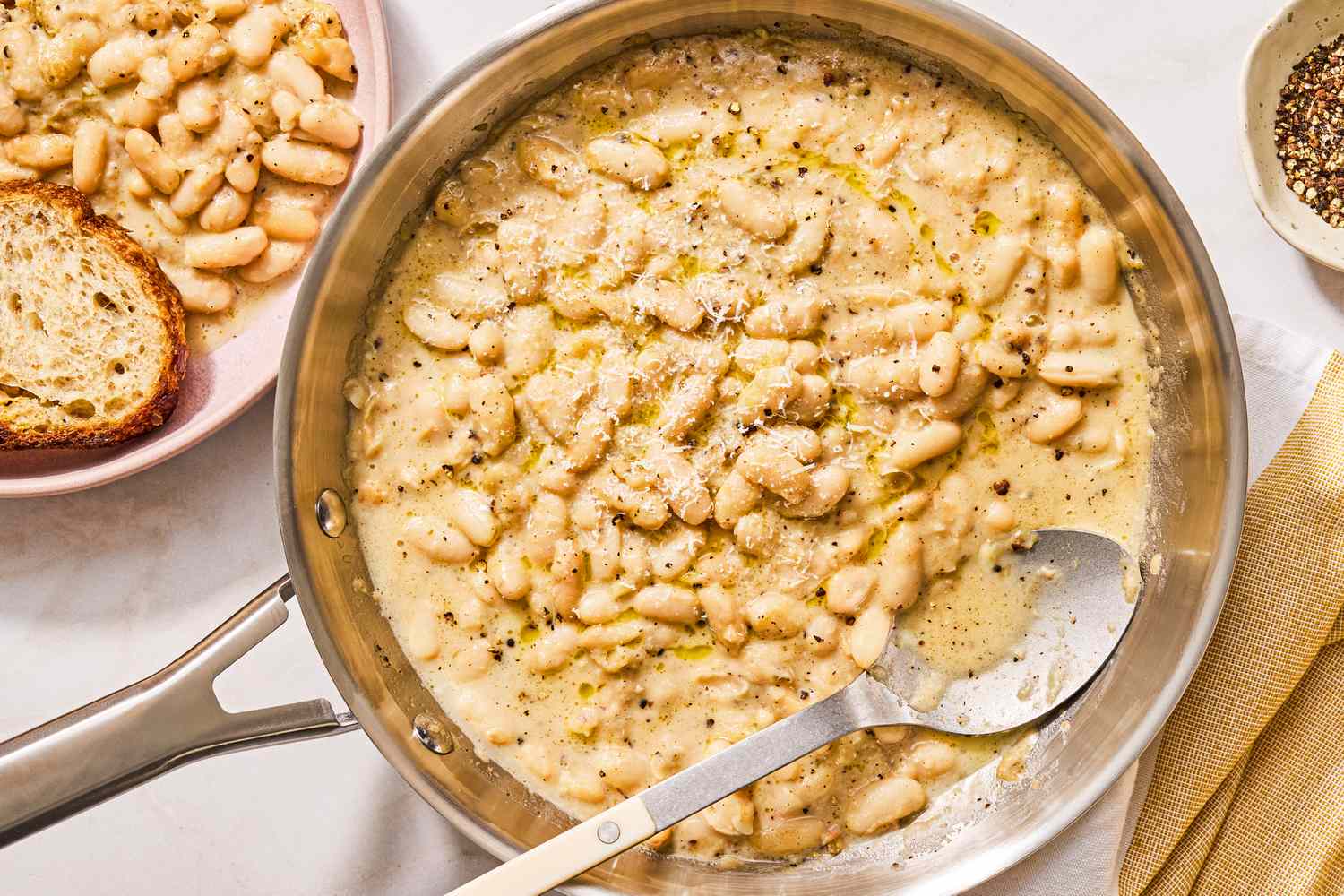 Pan of cacio e pepe style beans with a large spoon and slices of bread on the side
