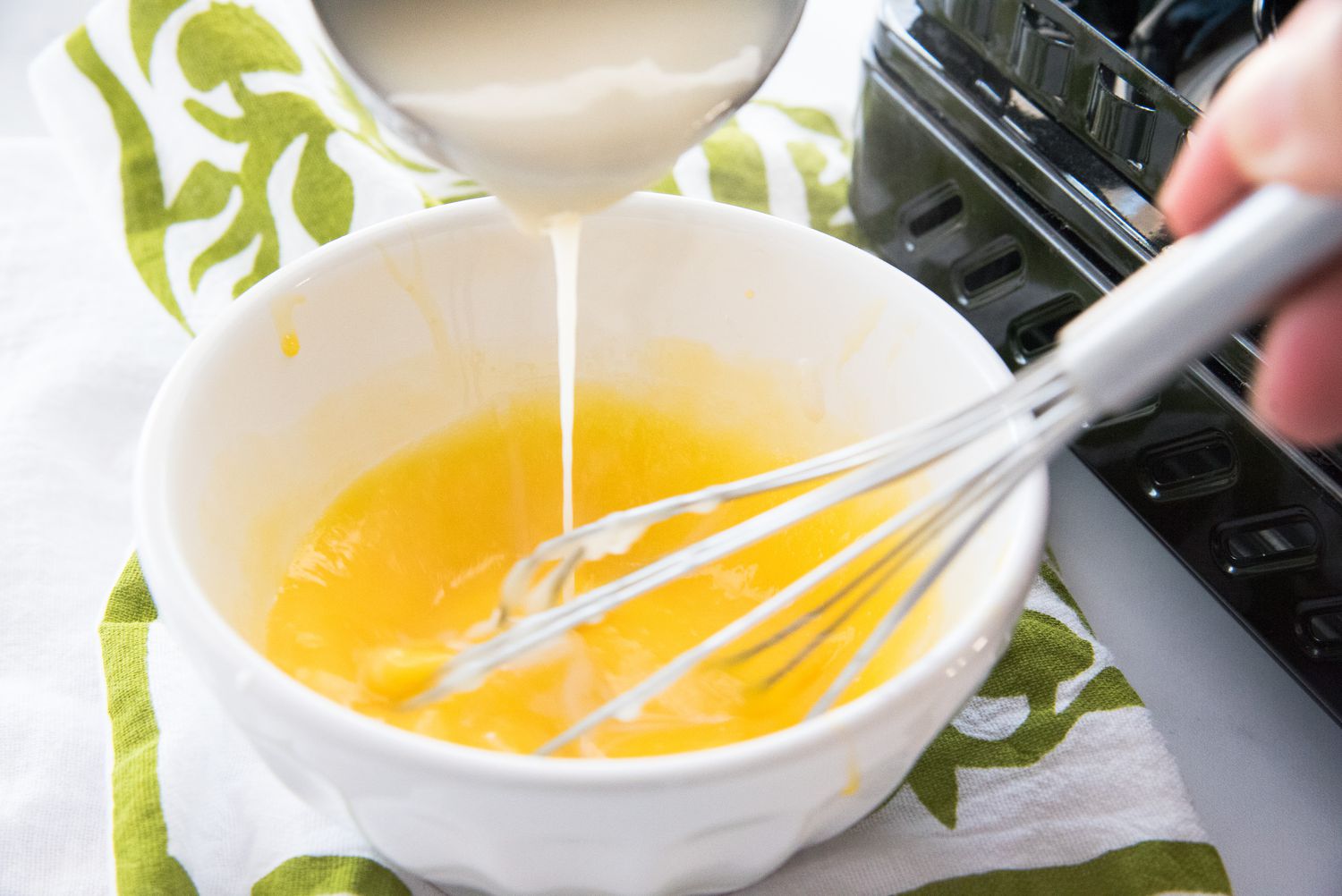 Adding cream to the egg mixture to make a German buttercream recipe.