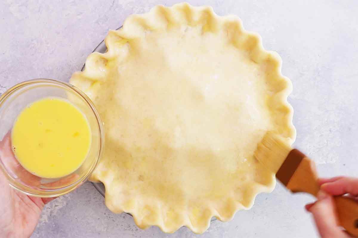 The top pie curst is being brushed with an egg wash