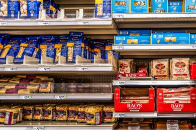 Grocery store shelf stocked with various brands of packaged pasta including Raos De Cecco and others