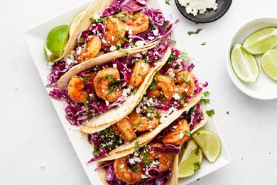 Blackened Shrimp Tacos and Lime Wedges on a Plate Surrounded a Bowl of More Lime Wedge and a Bowl of Queso Fresco