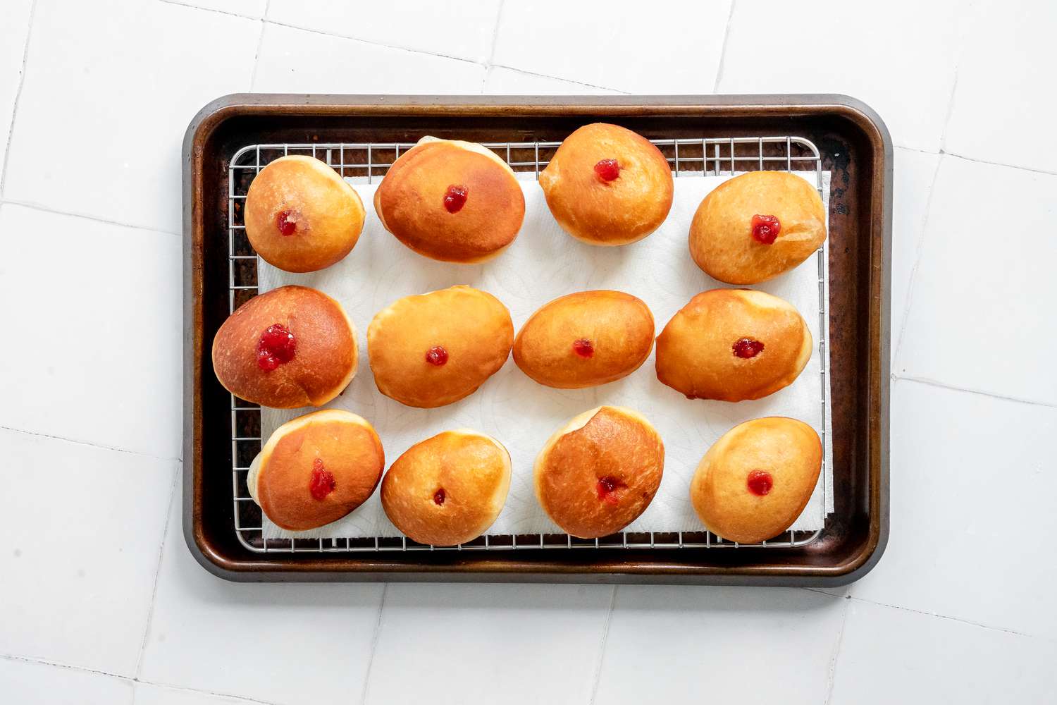 Sufganiyot (Israeli Jelly Donuts) Resting on a Paper Towel Lined Cooling Rack on a Baking Sheet