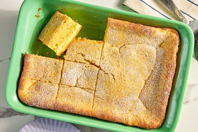 A baked cake in a green baking dish partially cut into squares