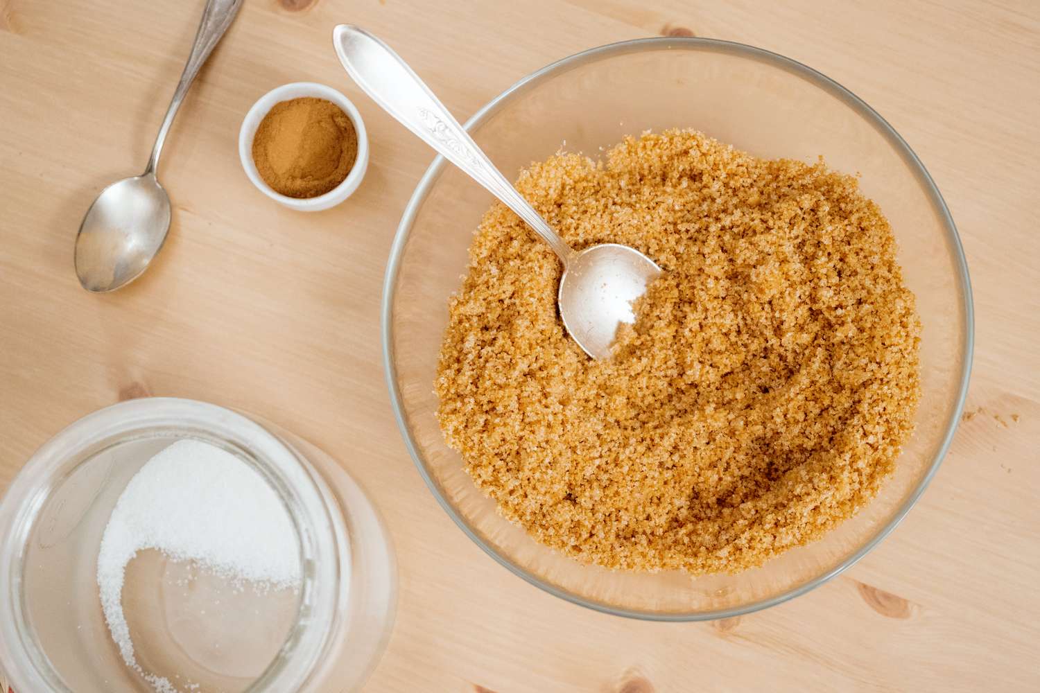 A bowl of brown sugar with a spoon next to a container of granulated sugar and a small dish of cinnamon