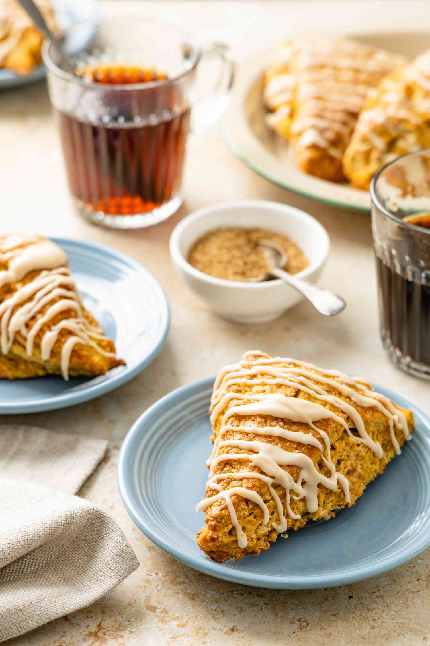Pumpkin Scones on Plate Surrounded by Cups of Coffee and a Bowl of Sugar