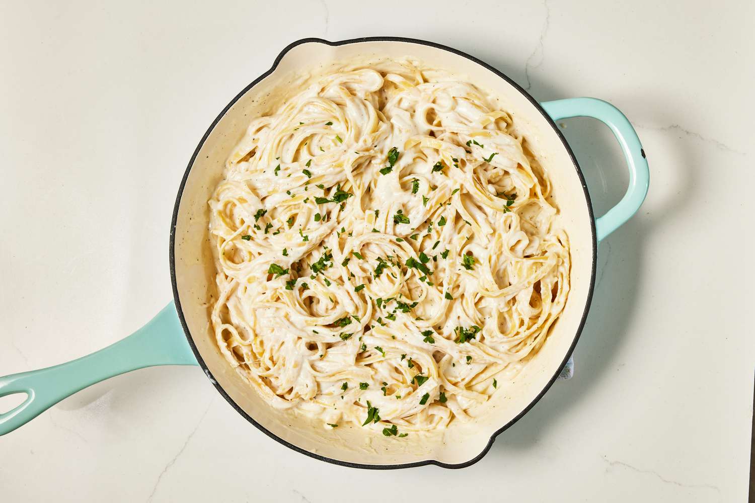 Skillet of copycat Olive Garden Alfredo topped with minced parsley