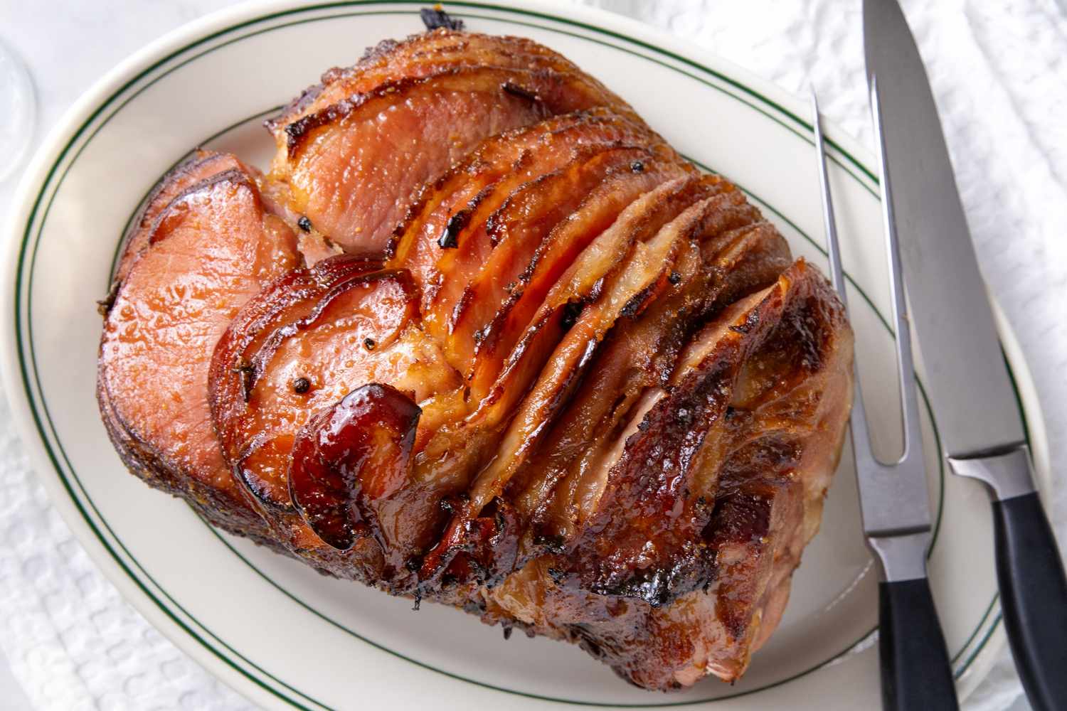 Sliced roasted ham served on a platter with a carving fork and knife beside it
