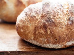 Side view of no-knead dutch oven bread on a cutting board. The crust is deep golden brown and a second loaf is behind the first.