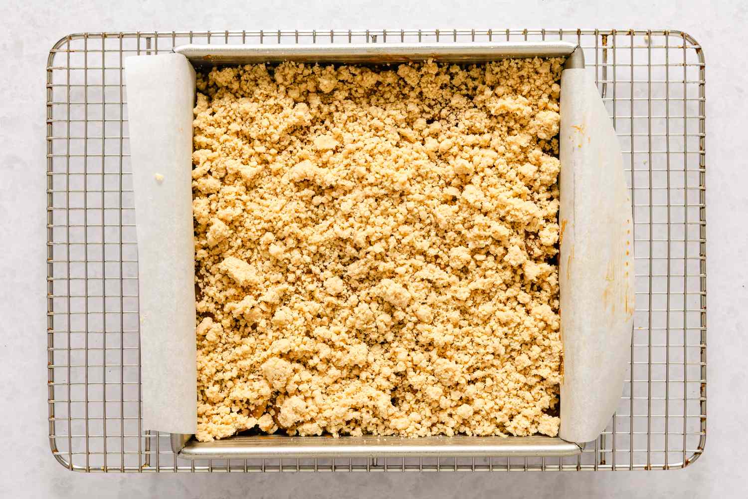 A square baking pan with caramel apple bars with streusel topping on a cooling rack