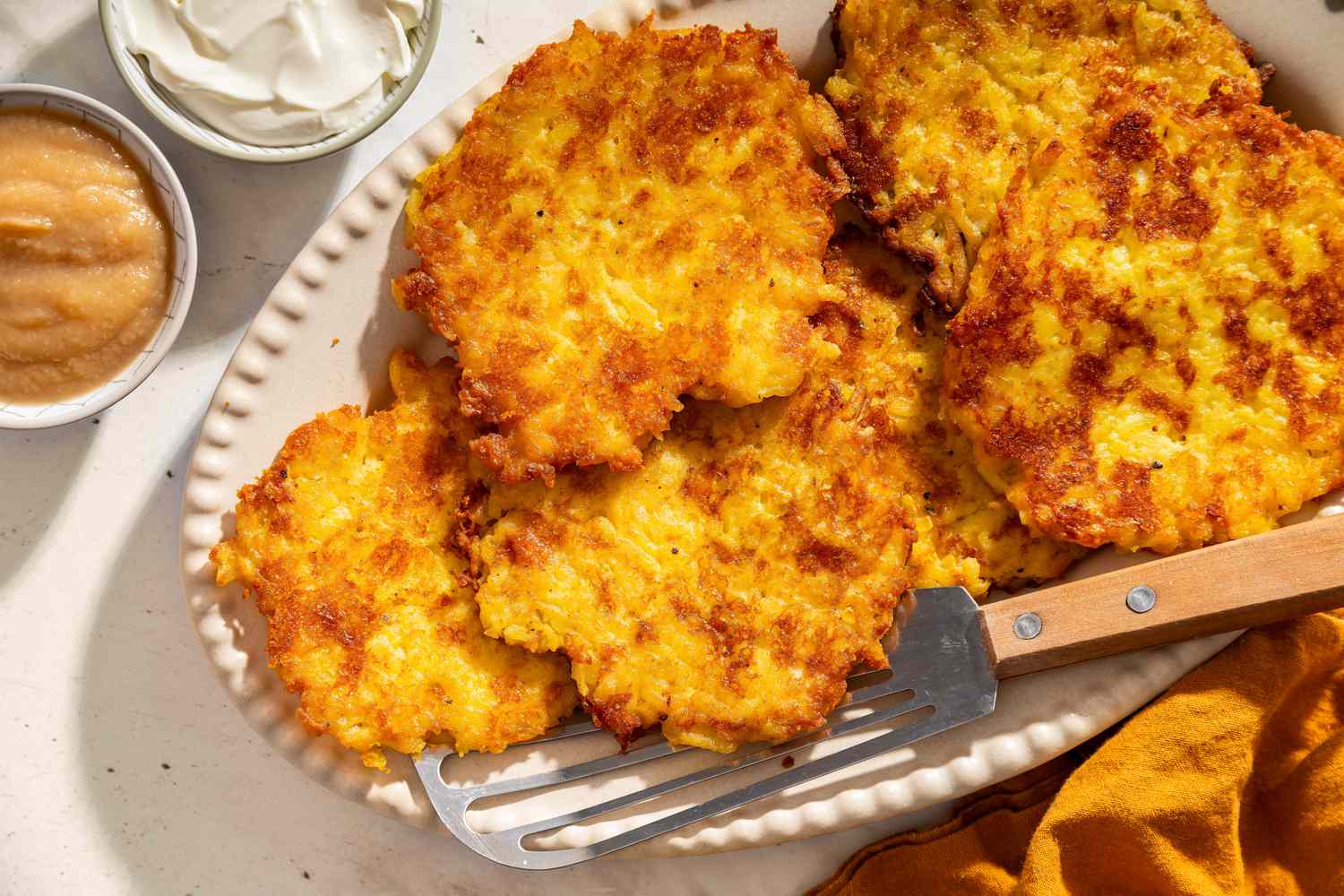 Plate of latkes with a spatula small bowls of sour cream and applesauce nearby