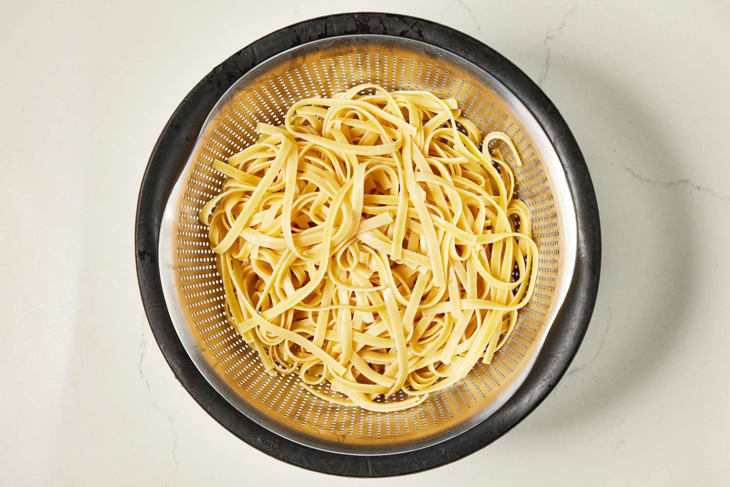 Cooked fettucine pasta in a colander for copycat Olive Garden Alfredo recipe