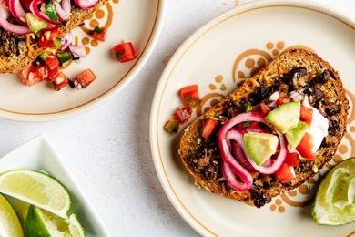 Black bean toast on a plate next to another plate with a serving and a bowl of lime slices