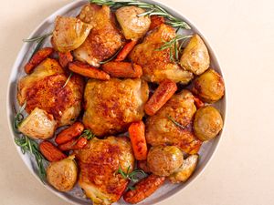 Roasted chicken thighs served with potatoes and carrots on a plate garnished with herbs