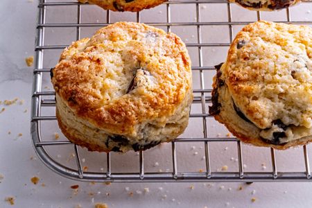 Two scones cooling on a wire rack displaying a baked exterior with visible pieces of dried fruit