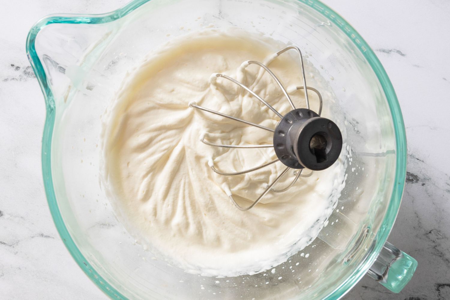 Whipped cream in a mixing bowl with a whisk attachment