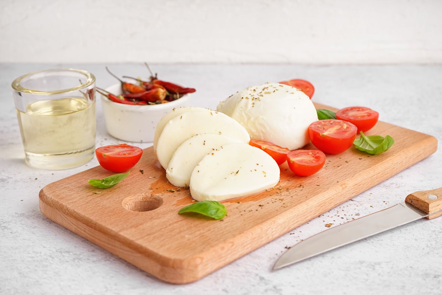Fresh Mozzarella Cheese, cherry tomatoes, and basil on a cutting board with a knife