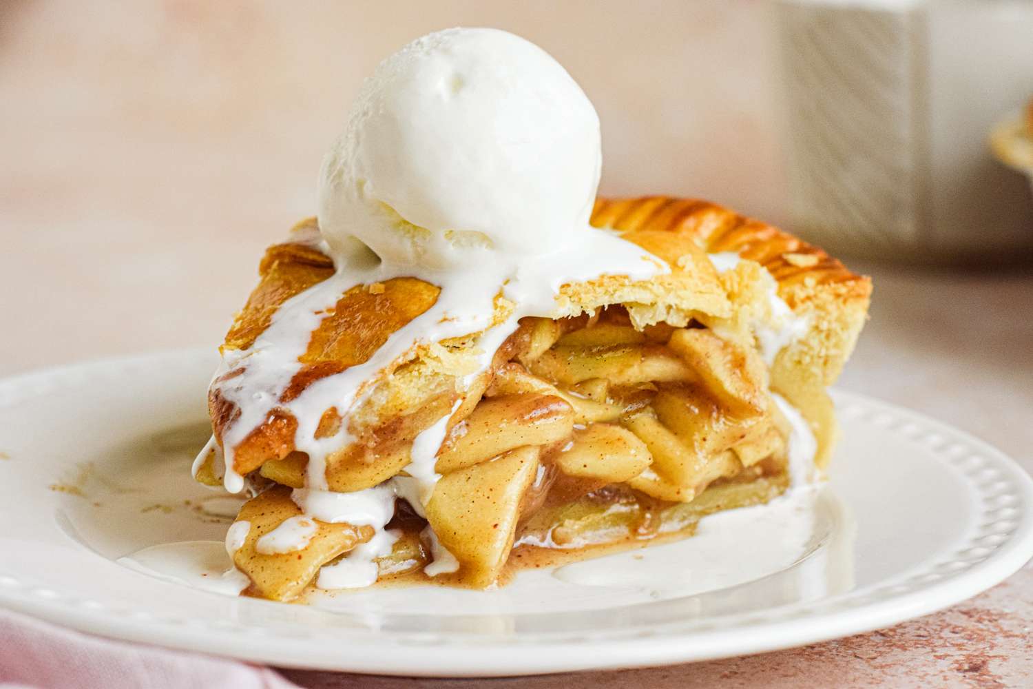Slice of apple pie topped with a scoop of vanilla ice cream on a white plate