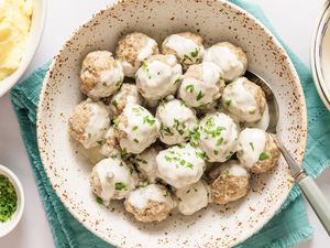 A bowl of meatballs covered in a creamy sauce garnished with parsley