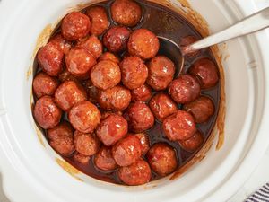 A slow cooker filled with meatballs in a sauce with a spoon for serving