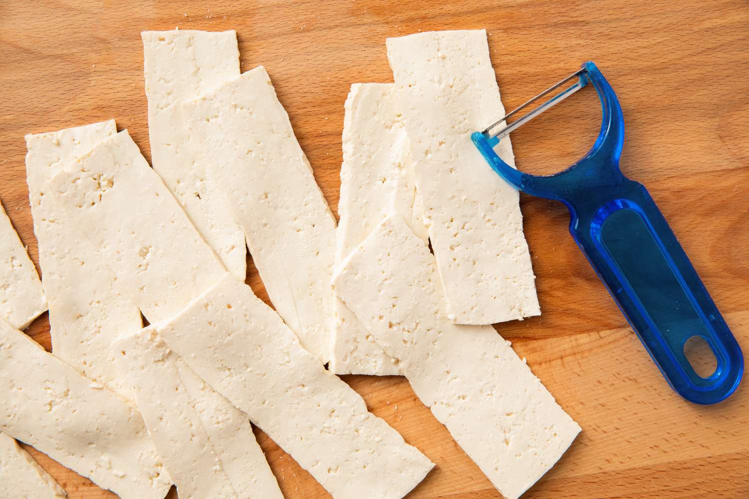 Thinly sliced tofu with a vegetable peeler on a wooden surface