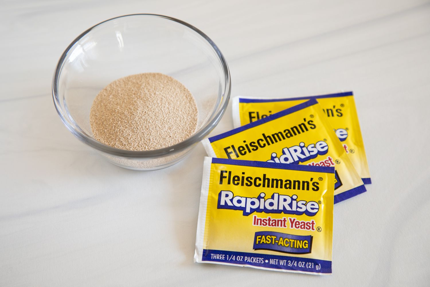 Three packages of yeast next to a small glass bowl with yeast inside.