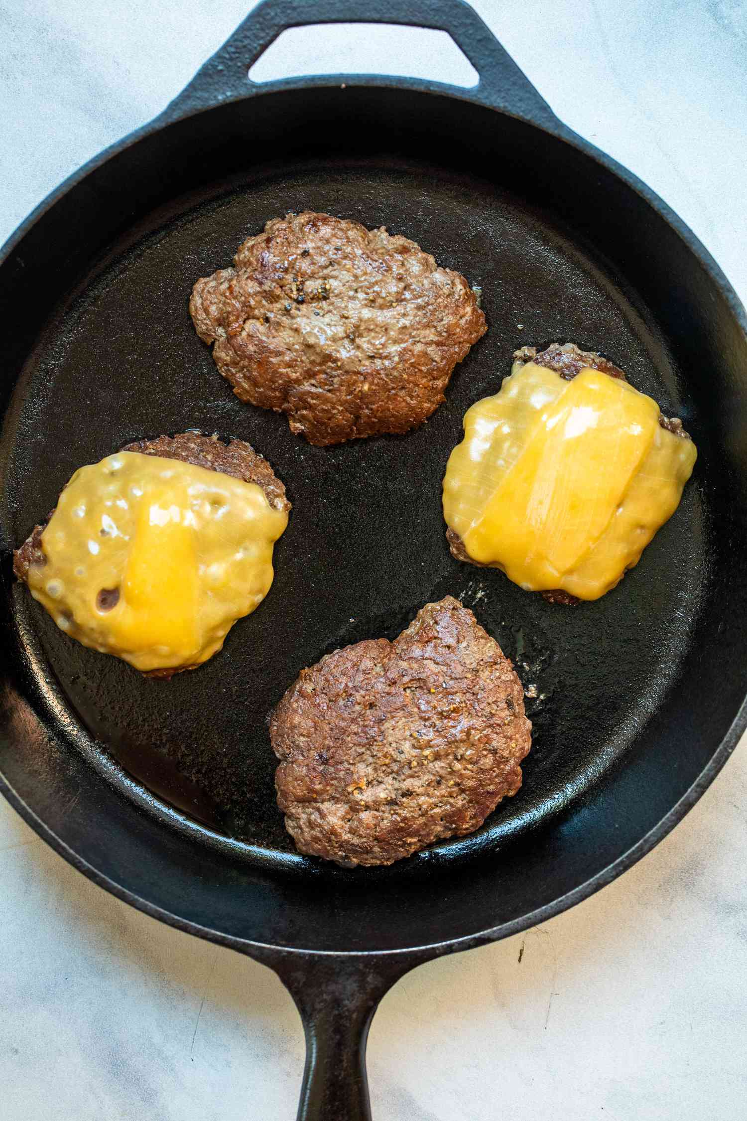Four Burgers on a Cast Iron Skillet with Two Patties Covered in Melted Cheese