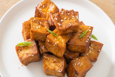 Tofu cubes garnished with sesame seeds and green onions on a white plate