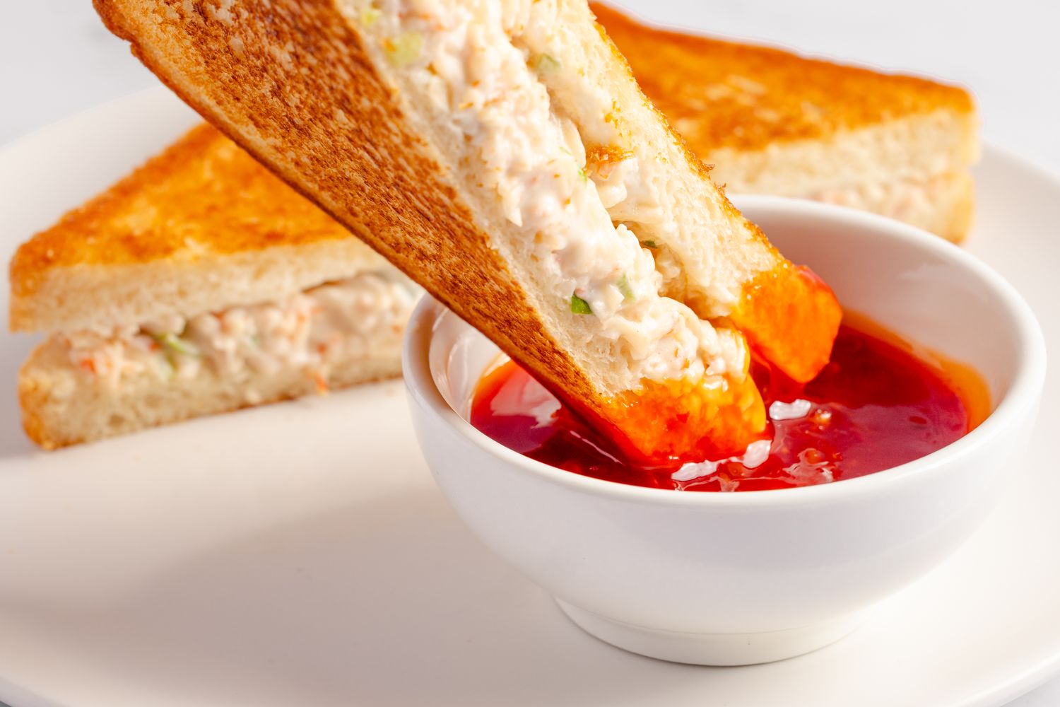 Crab rangoon sandwich being dipped into sauce on a white plate