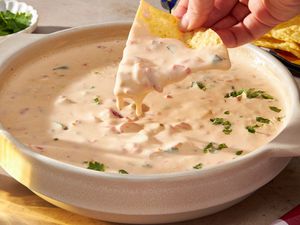 Corn chip with chile con queso cascading off it into a bowl with more chile con queso (at a table setting)