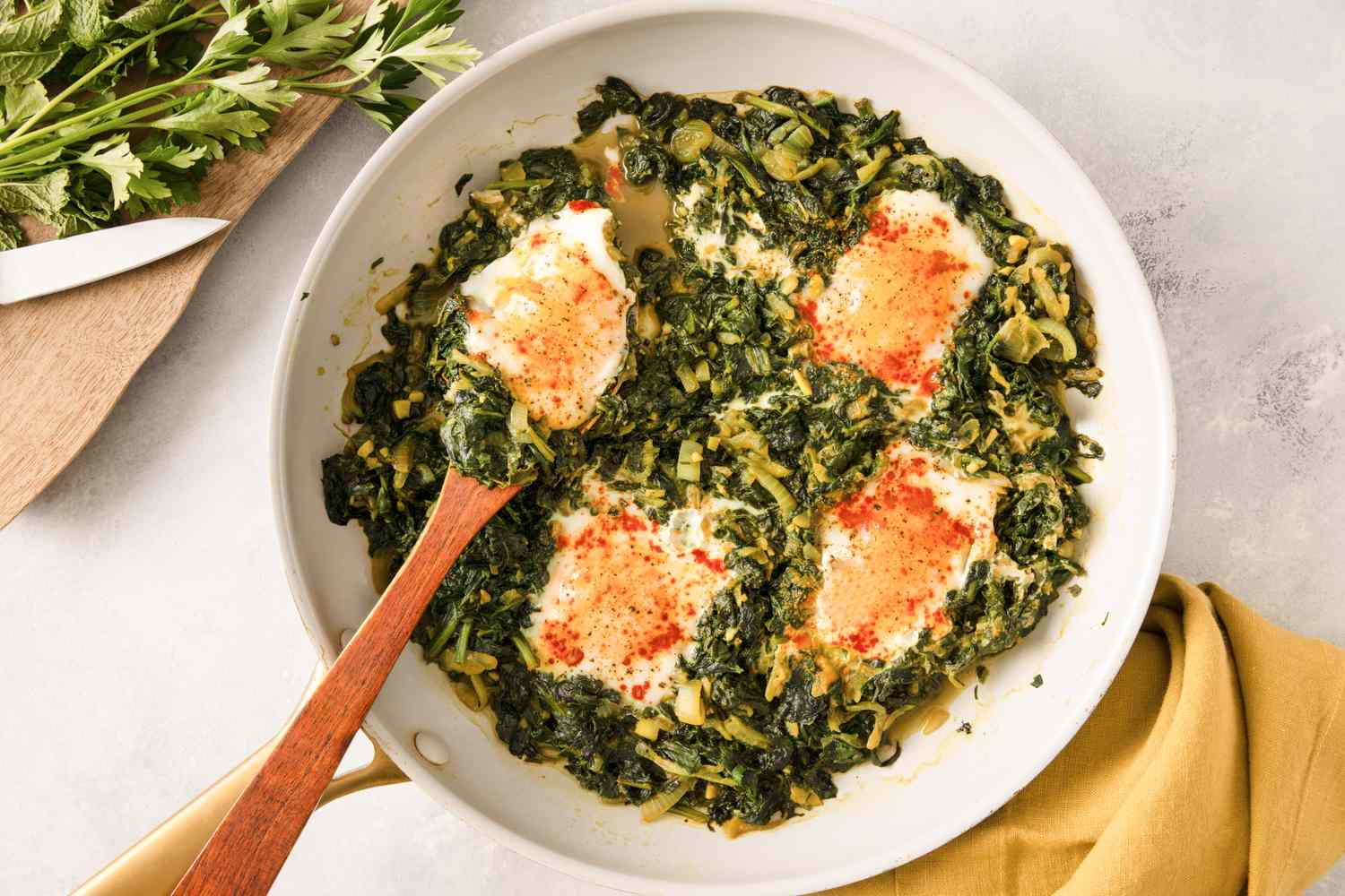 A skillet containing a dish of sauted greens with poached eggs garnished with a spice or seasoning