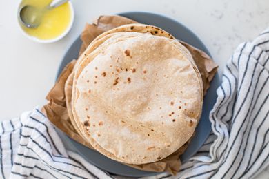 Overhead view of a stack of Indian flatbread roti on a plate with a striped linen underneath.