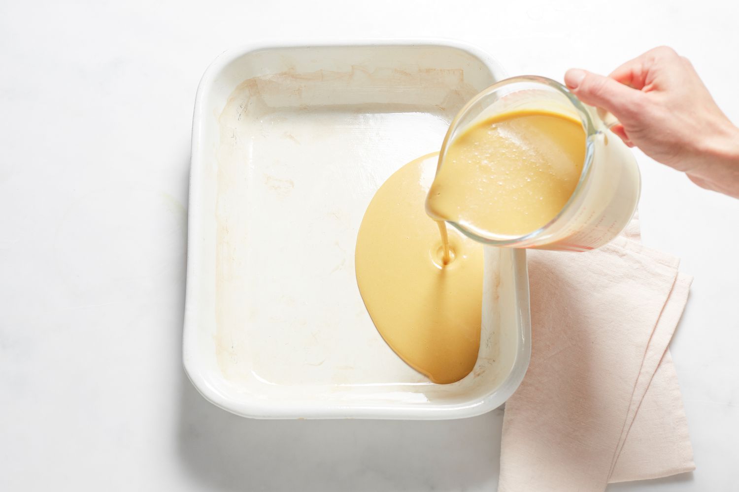 Pouring batter and spreading bean paste on a Sticky rice cake with red bean paste in a baking dish.