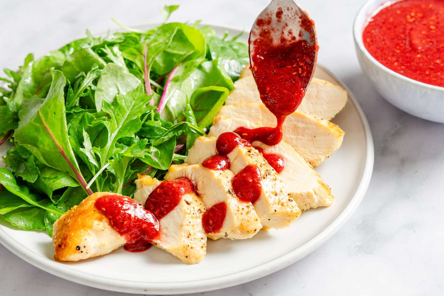 Raspberry-Soy Sauce in a small bowl with a spoon drizzling on pieces of chicken