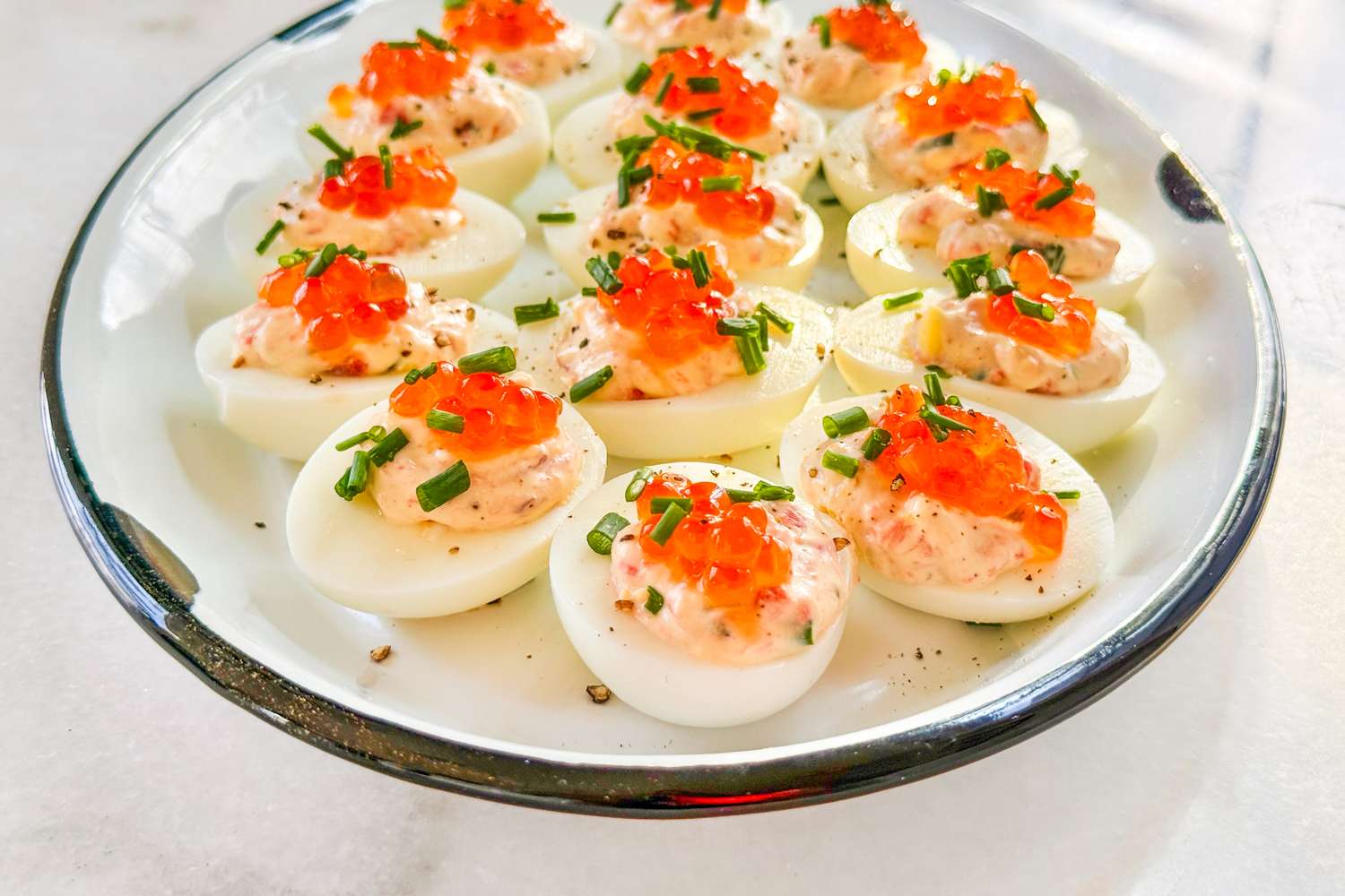 A plate of deviled eggs topped with red garnish and herbs