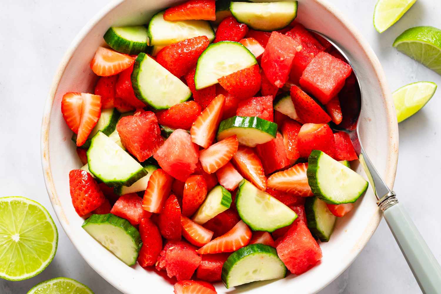 large bowl of Hydration Salad with a serving spoon, lime wedges on the side