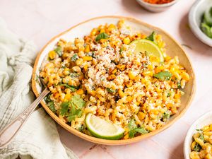 A bowl of esquites pasta salad garnished with lime wedges and cilantro