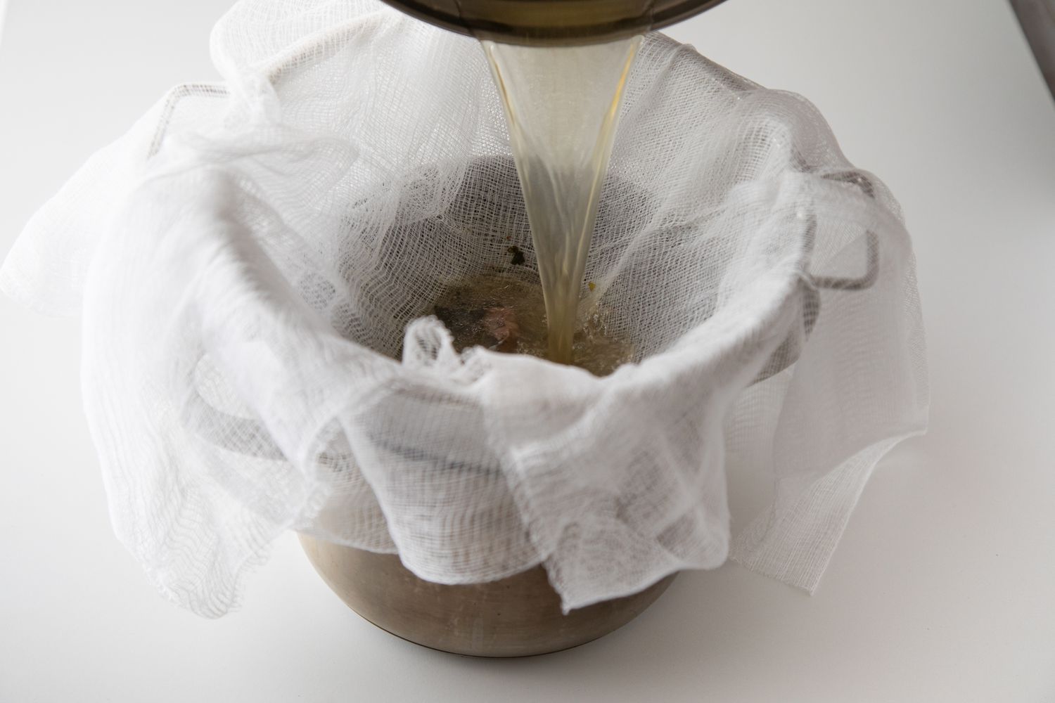 Straining beef broth through cheesecloth.