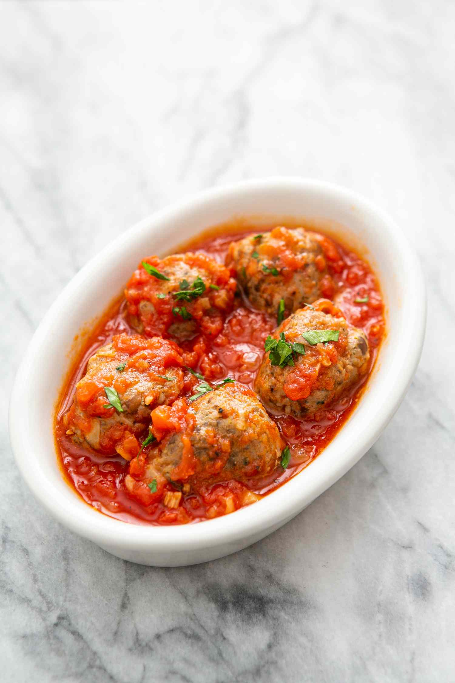 Turkey Meatballs in Tomato Sauce and Topped With Basil in a White Dish