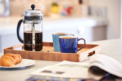 Coffee brewed in cafetiere on the kitchen work top with two mugs and a plate with a croissant