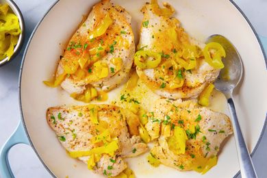 A skillet with cooked chicken breasts topped with banana peppers and garnished with herbs