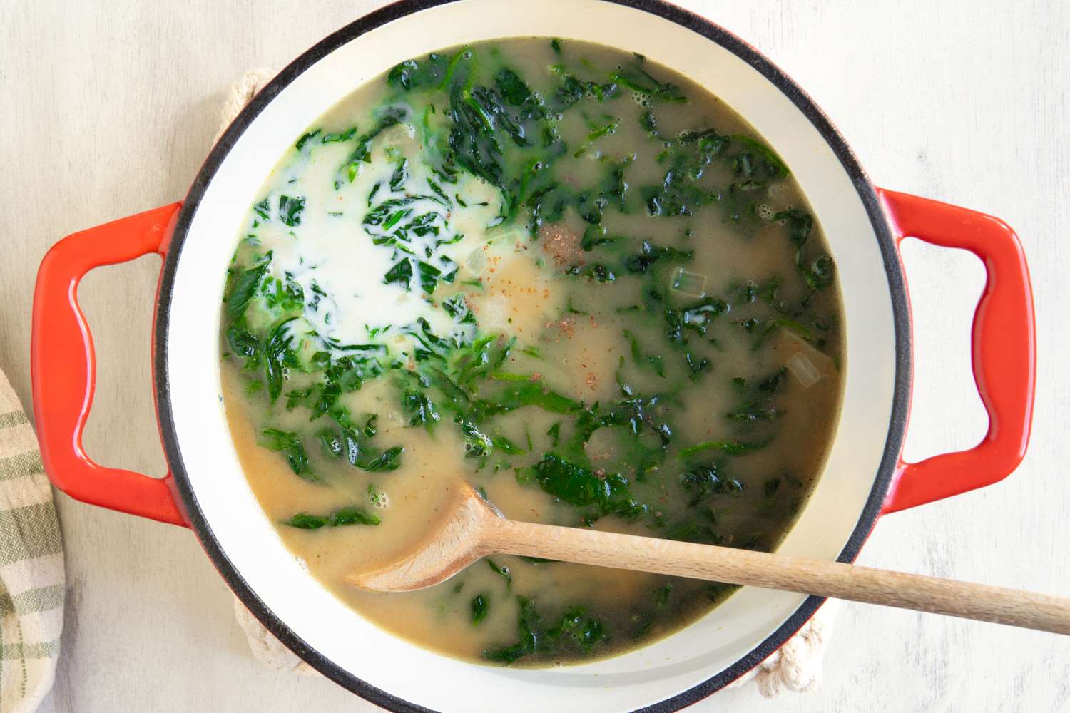 A pot of soup containing spinach and other ingredients with a wooden spoon resting inside