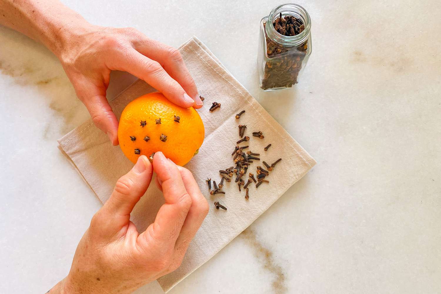 hands pushing cloves into an orange
