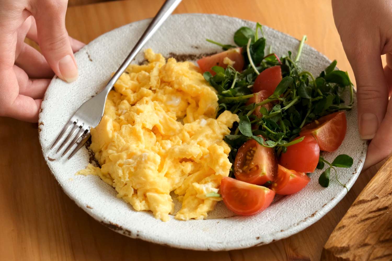 A plate of scrambled eggs with a pea shoot and tomato salad